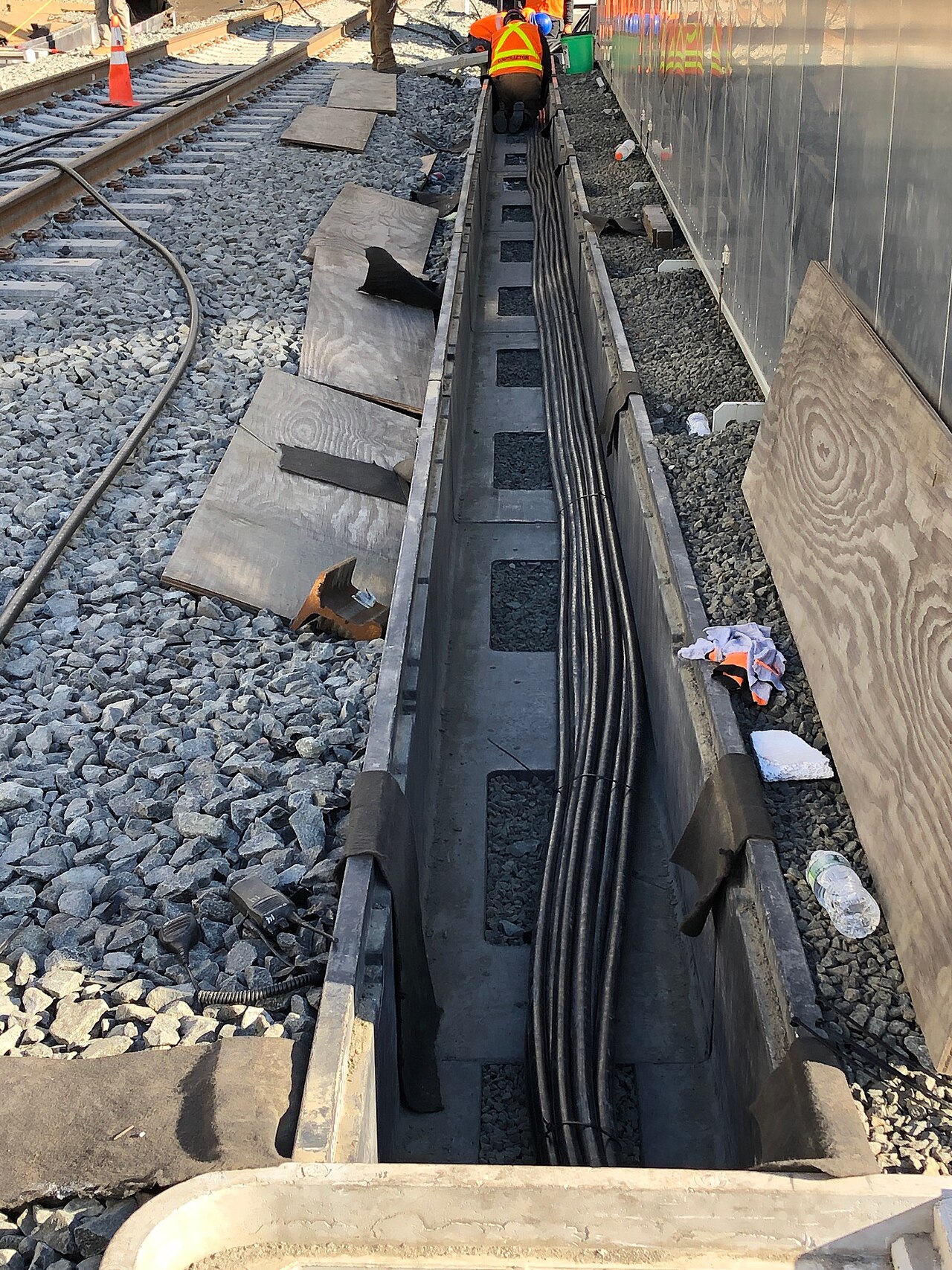 Beschäftigte legen Signalkabel in einen offenen Kabeltrog neben Bahngleisen