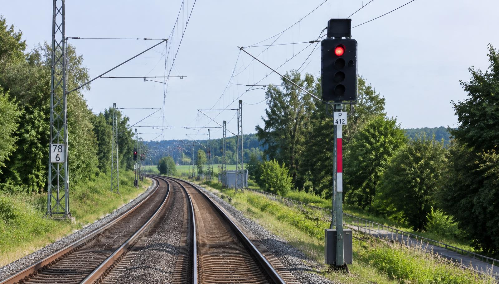 Signalmast mit rotem Licht neben einem elektrifizierten Gleis