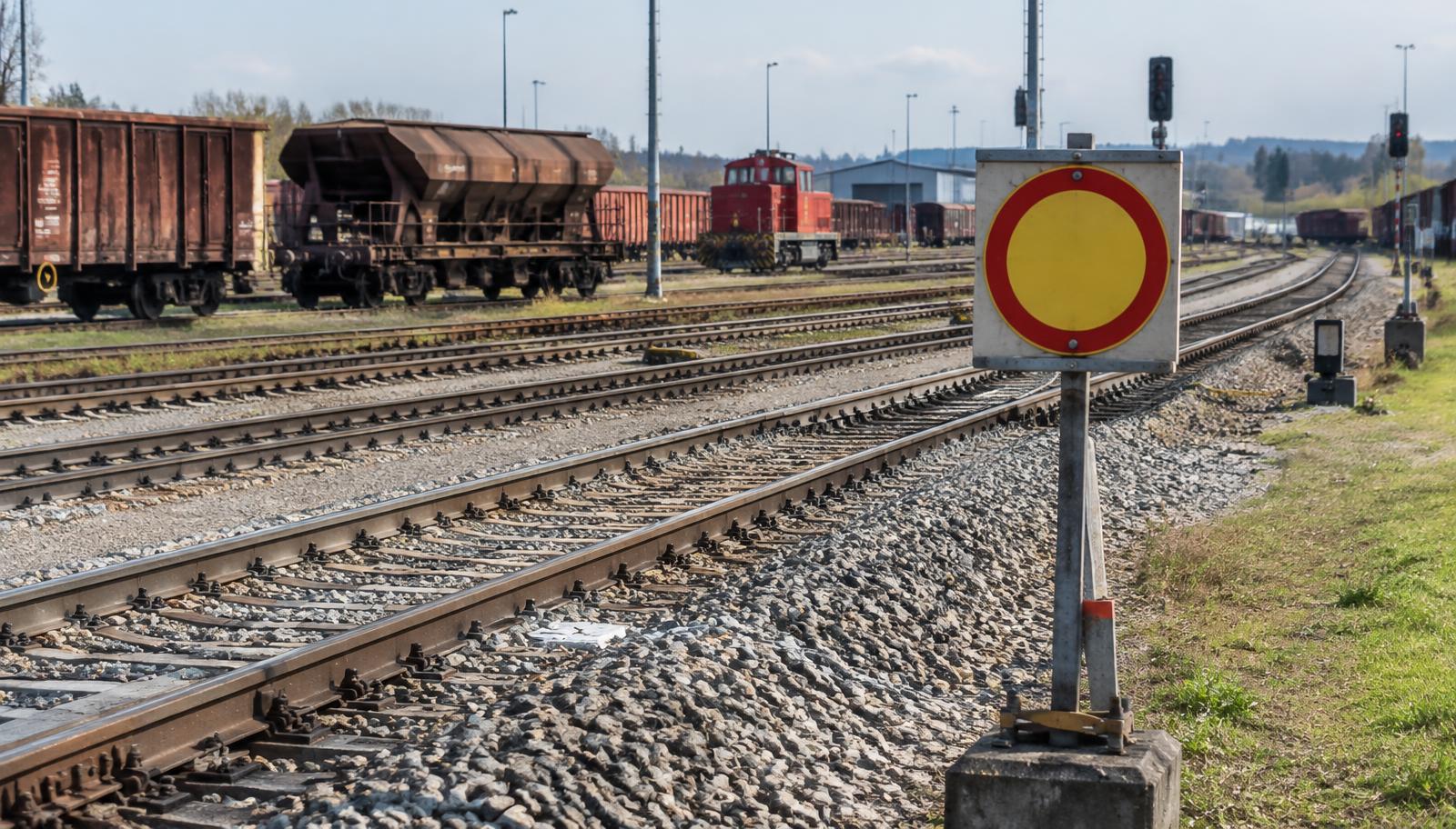 Gelbe runde Signaltafel auf einem Mast neben dem Gleis, im Hintergrund abgestellte Güterwagen